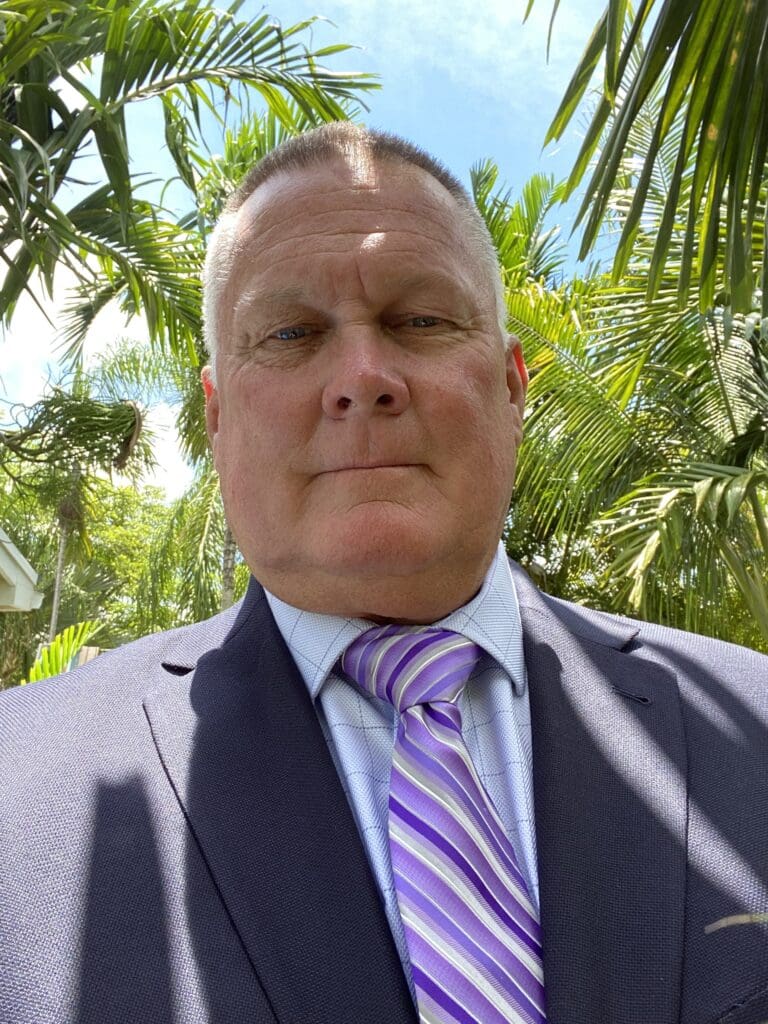 A man in a suit and tie standing under some trees.