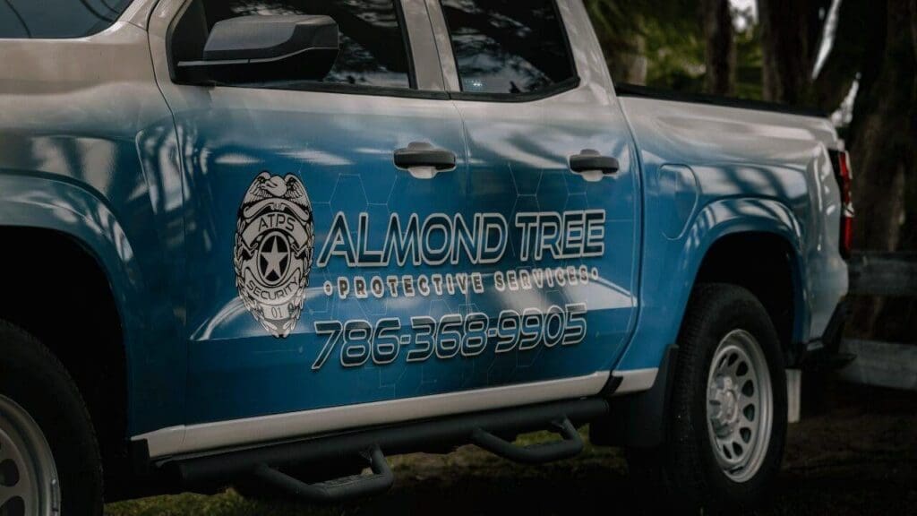 Side of a blue Almond Tree Protective Services patrol truck showing the company badge logo and phone number