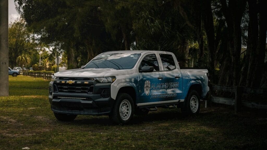 Marked Almond Tree security patrol truck parked on grass beside a tree line