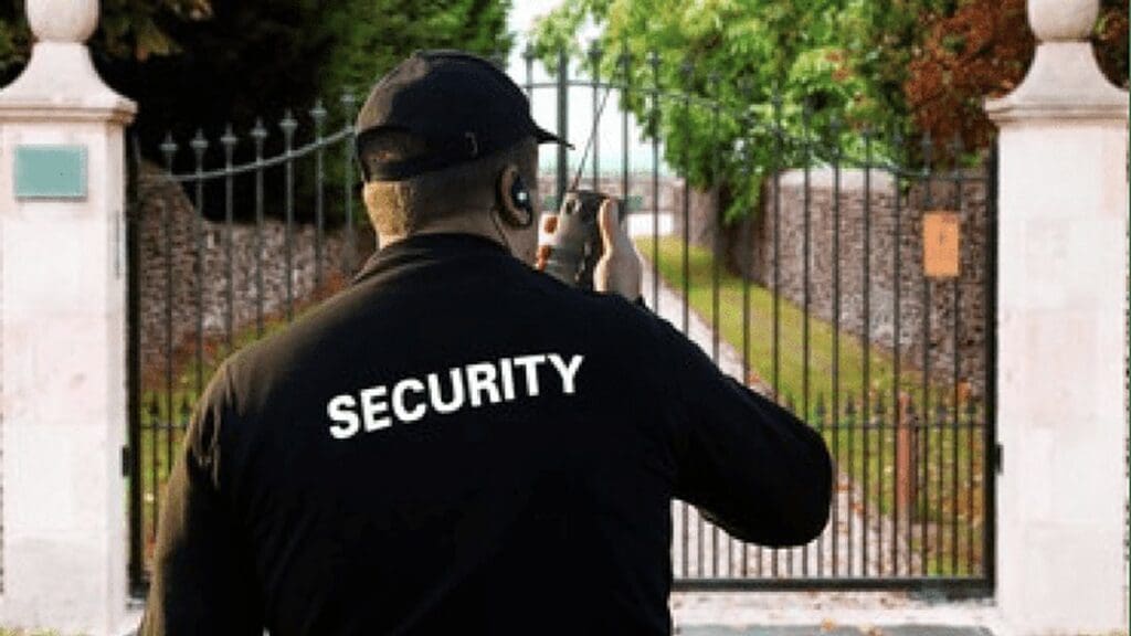 Security officer with a radio standing at the closed gate of a residential property